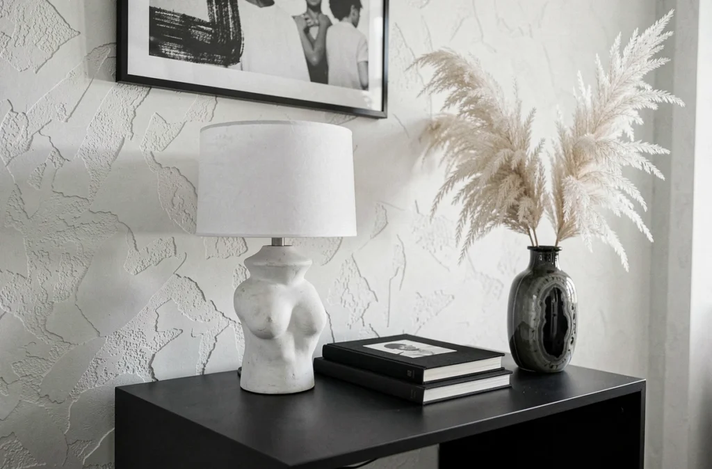 Détail décoratif d'un coin salon noir et blanc avec lampe en plâtre blanc, livres d'art et vase en céramique onyx